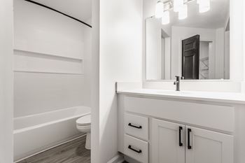 A white bathroom with a tub, sink, and mirror